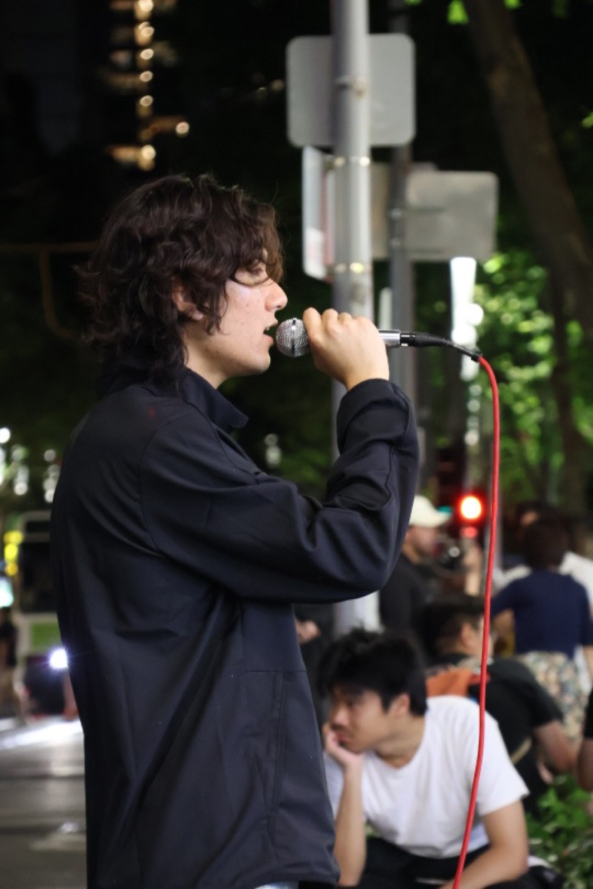 KUMA singing on a Melbourne street at night, seen in profile with the microphone cable visible.