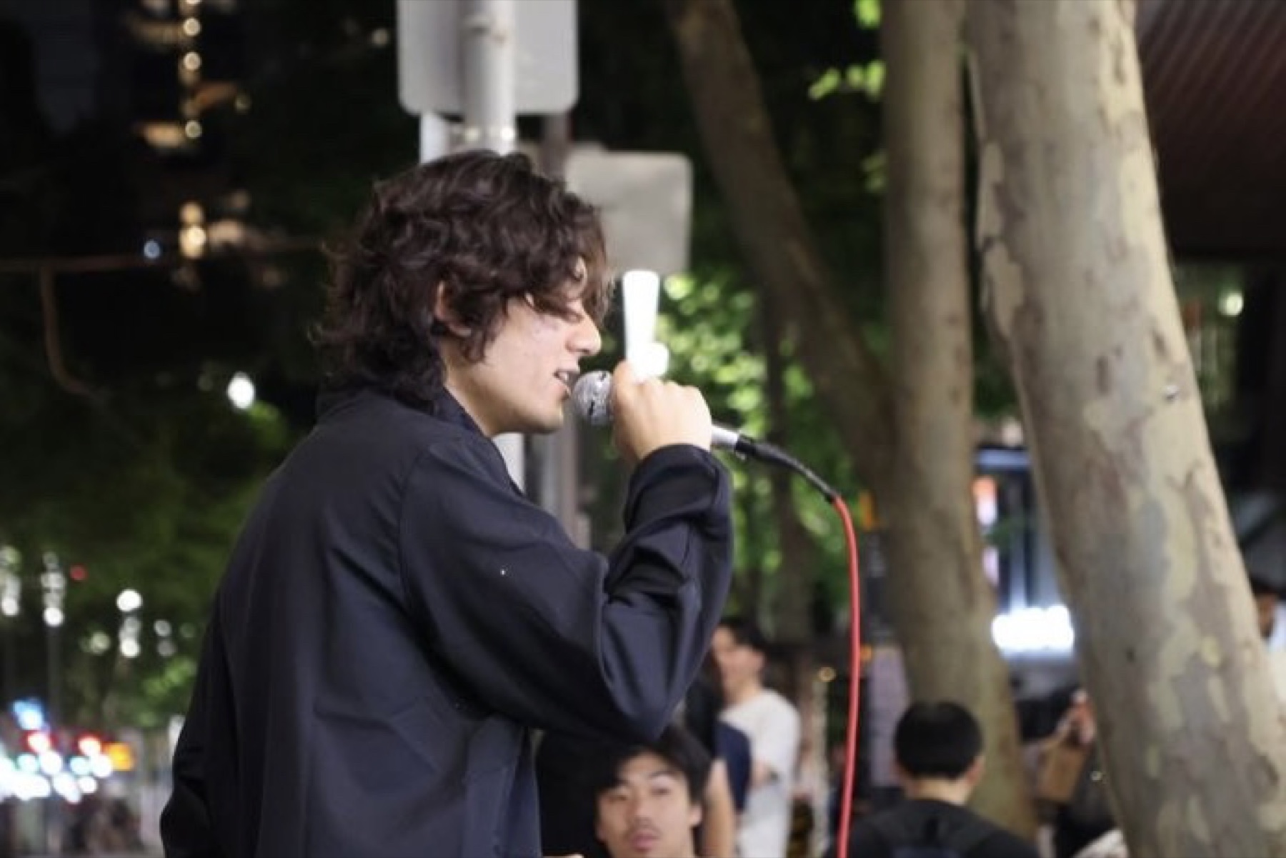 A closer street-side view of KUMA performing beneath trees at night.