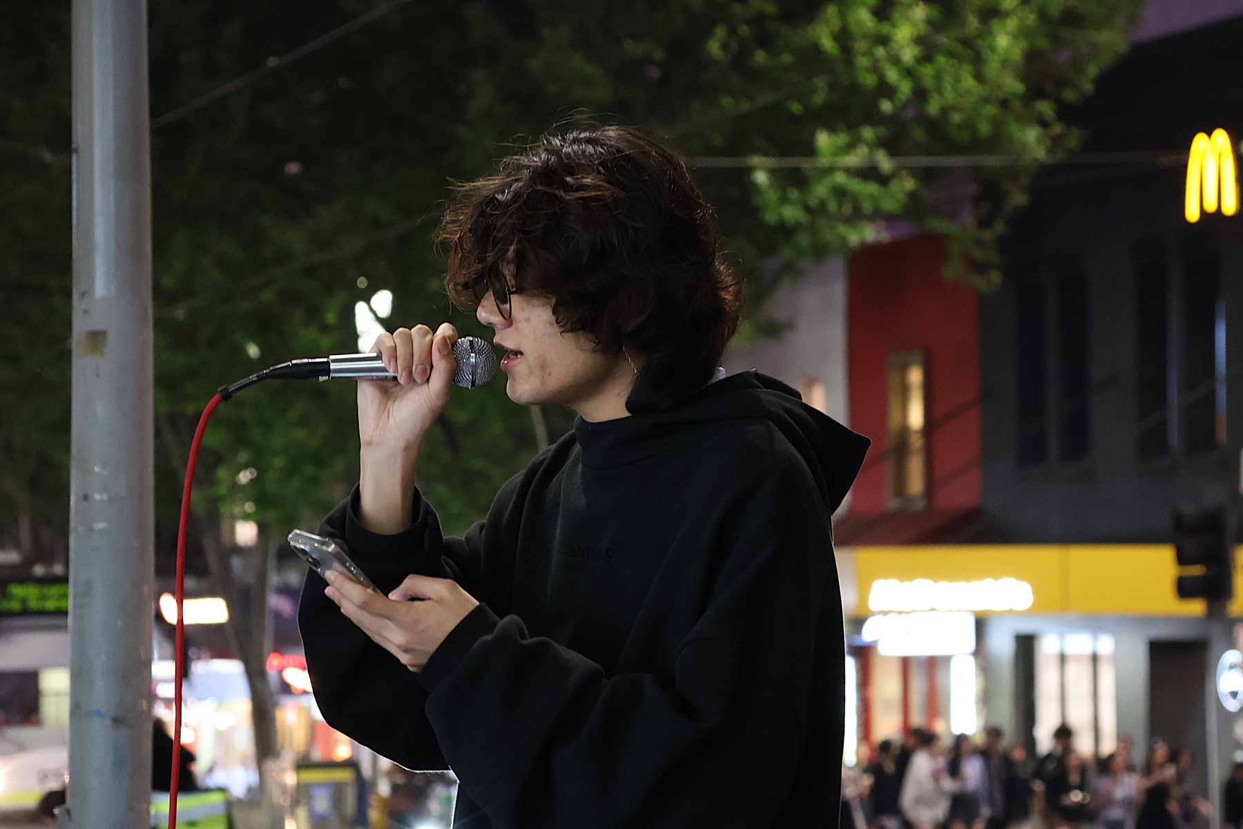 A close-up of KUMA singing into a microphone during a night-time street performance.
