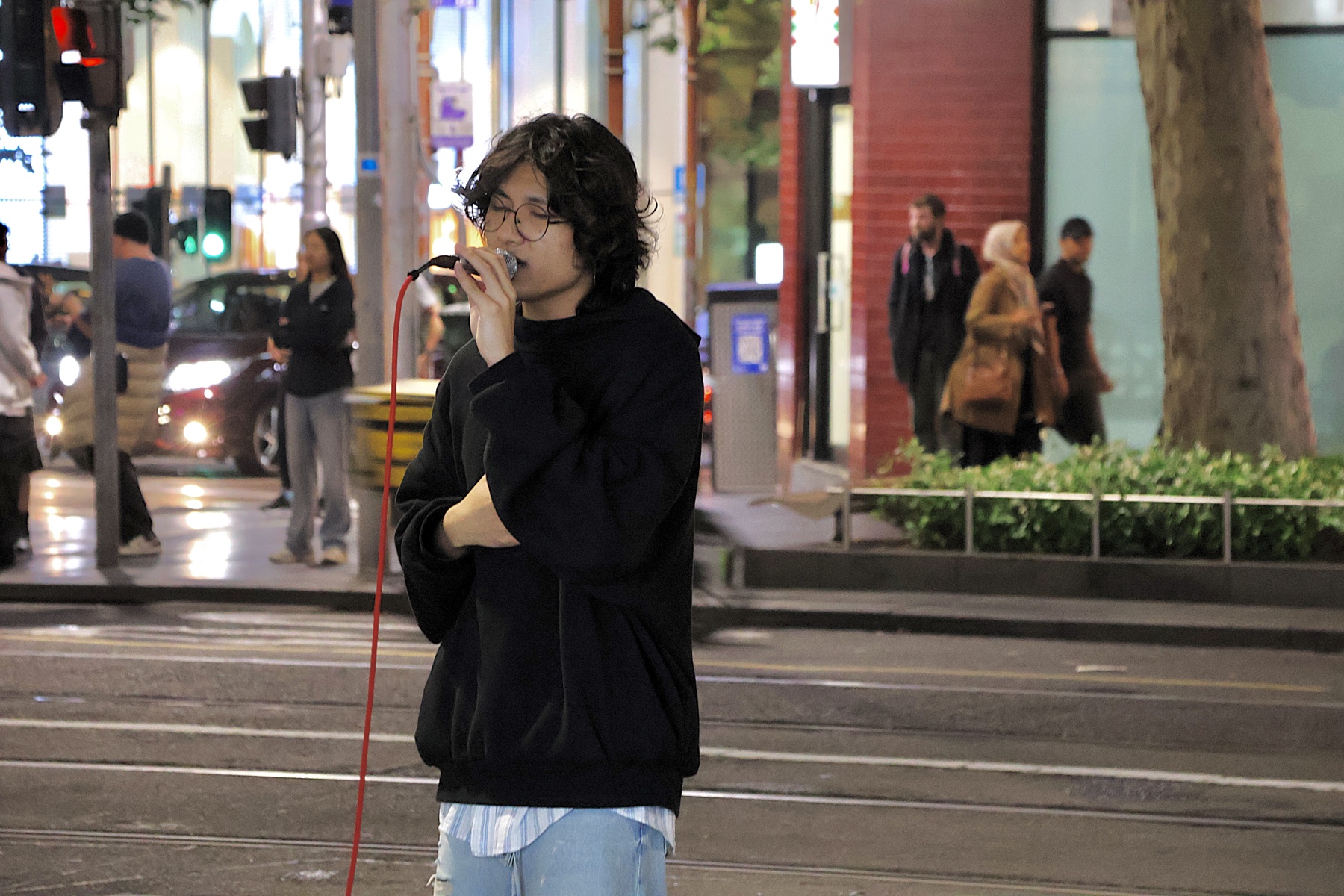 KUMA singing on a Melbourne street at night with trees and city lights in the background.