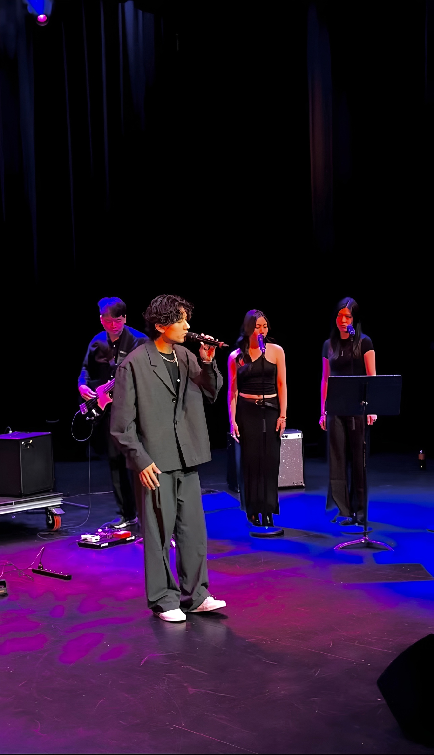 KUMA performing with backing vocalists under purple stage lights.