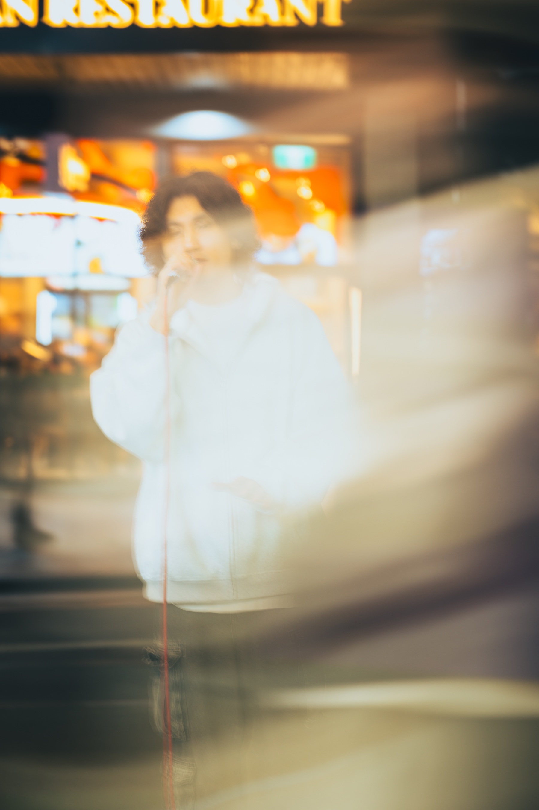 KUMA singing into a microphone against the amber lights of a Melbourne shopfront.