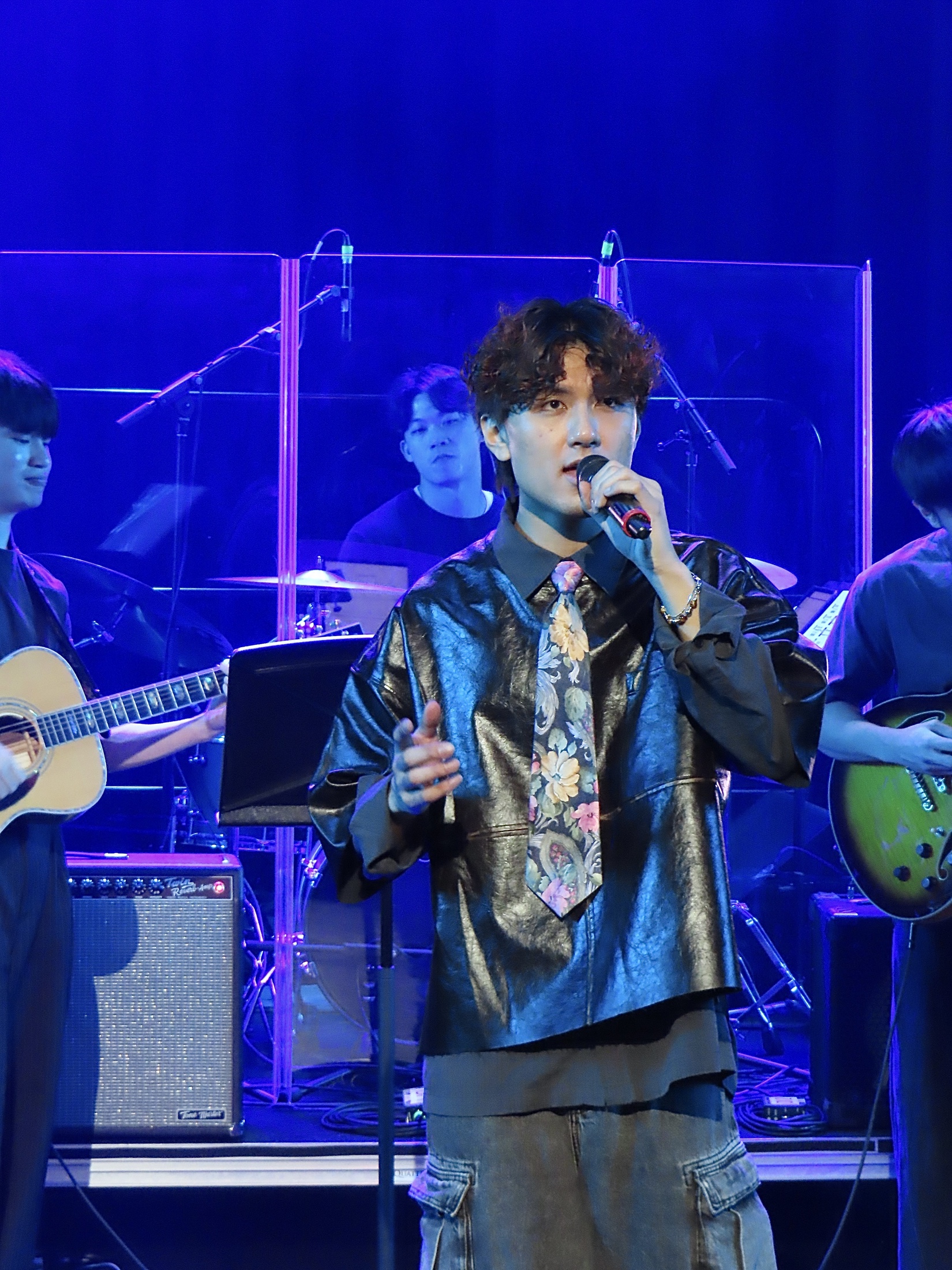 A close portrait of KUMA singing into the microphone beneath blue and violet lights.