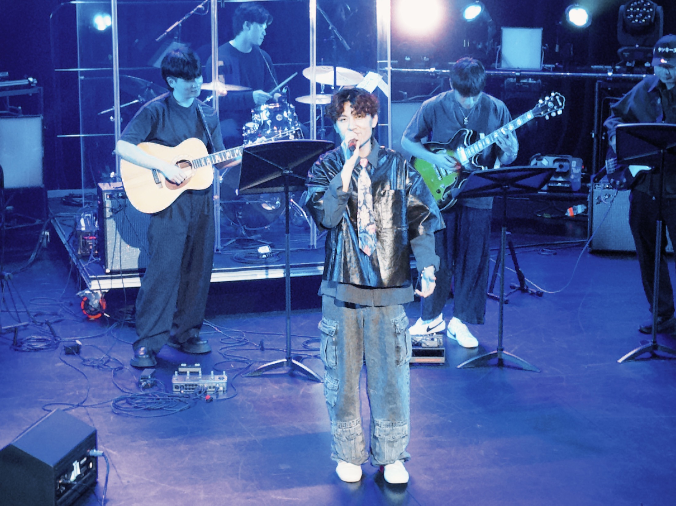 An elevated view of KUMA and the band performing in cool blue light.