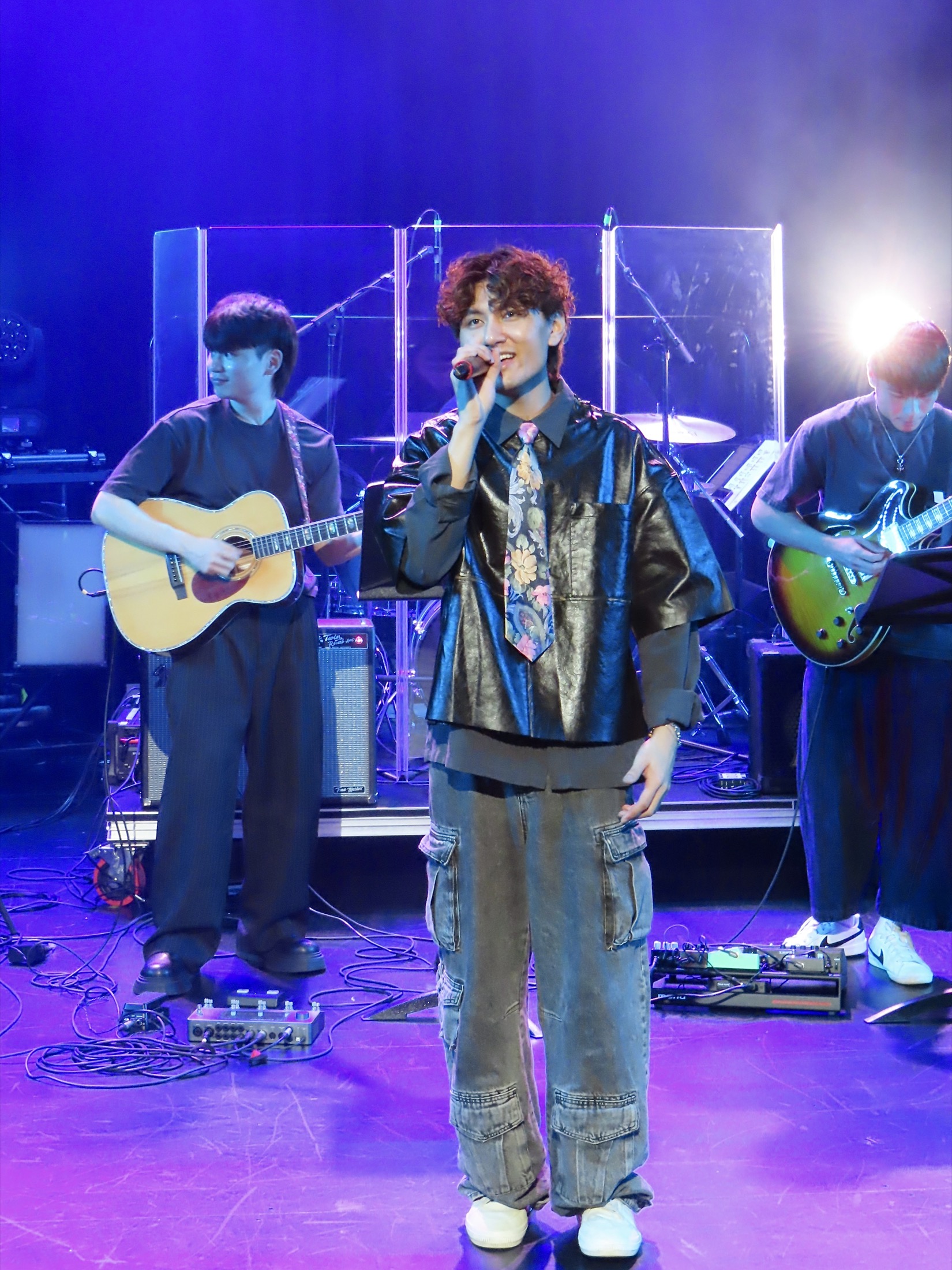 KUMA smiling into the microphone with the band behind him.