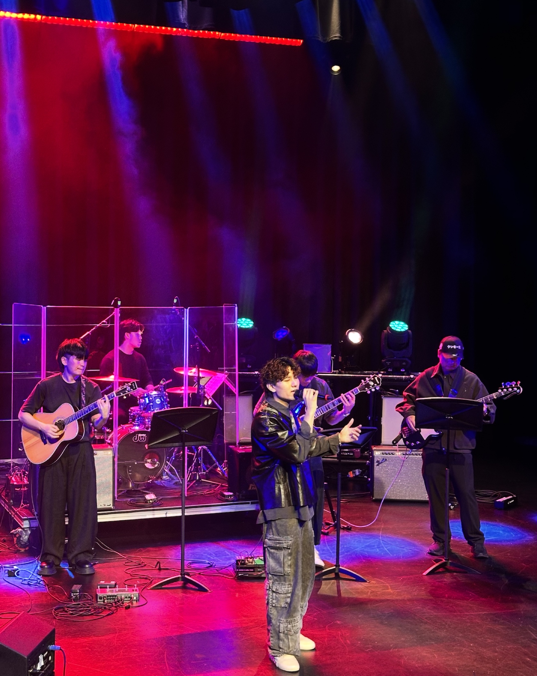 KUMA and the full band performing under red, magenta and blue lights.