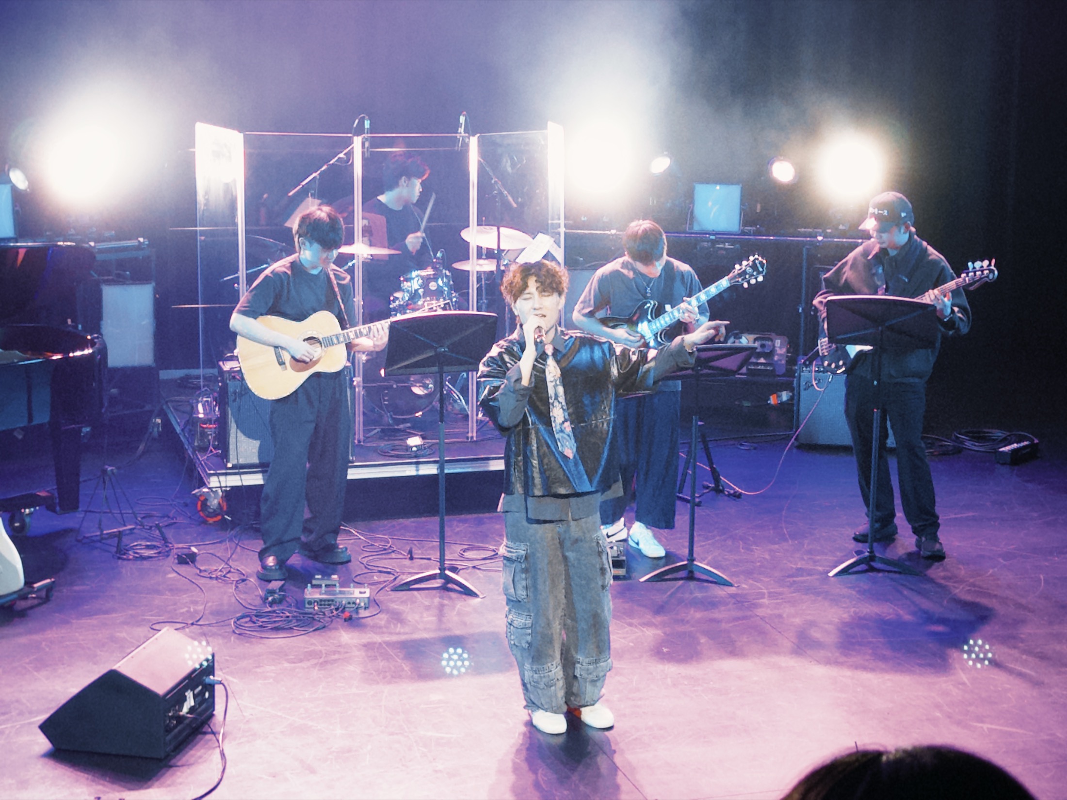 KUMA reaching toward the audience with the full band under pale violet lights.