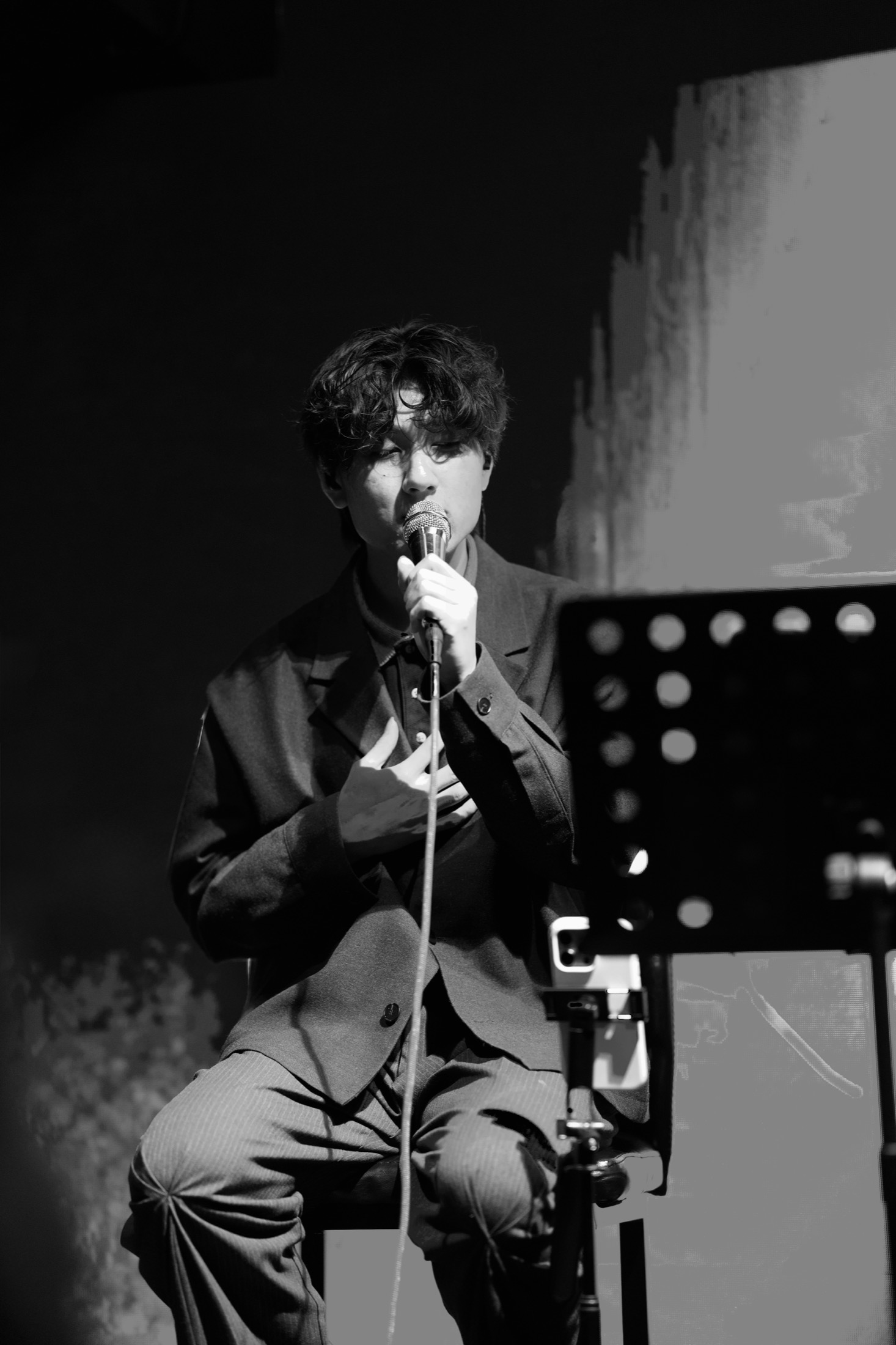 KUMA singing with a hand on his chest, photographed in black and white.