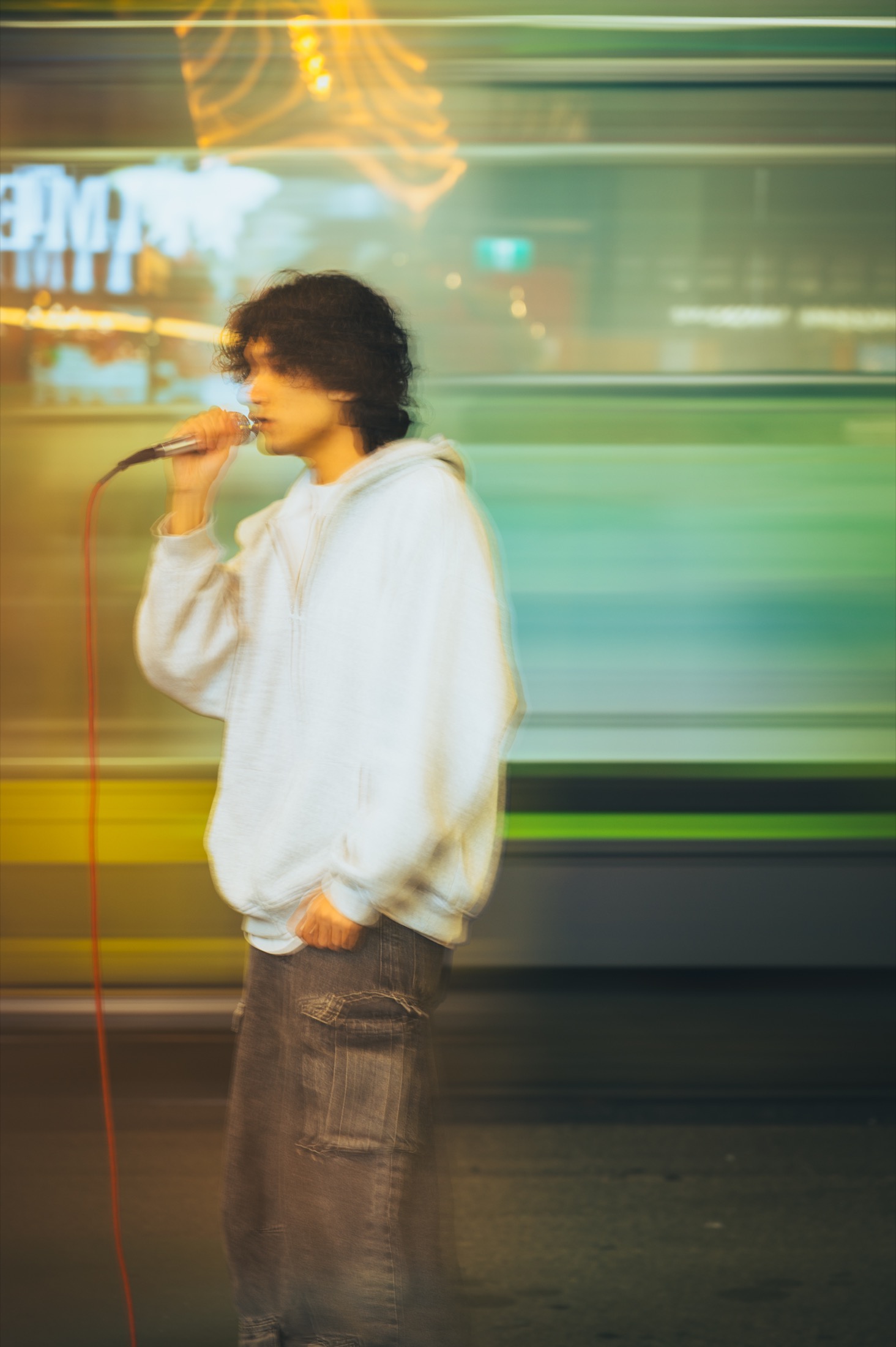KUMA busking on a Melbourne street, singing into a handheld microphone under warm city lights.