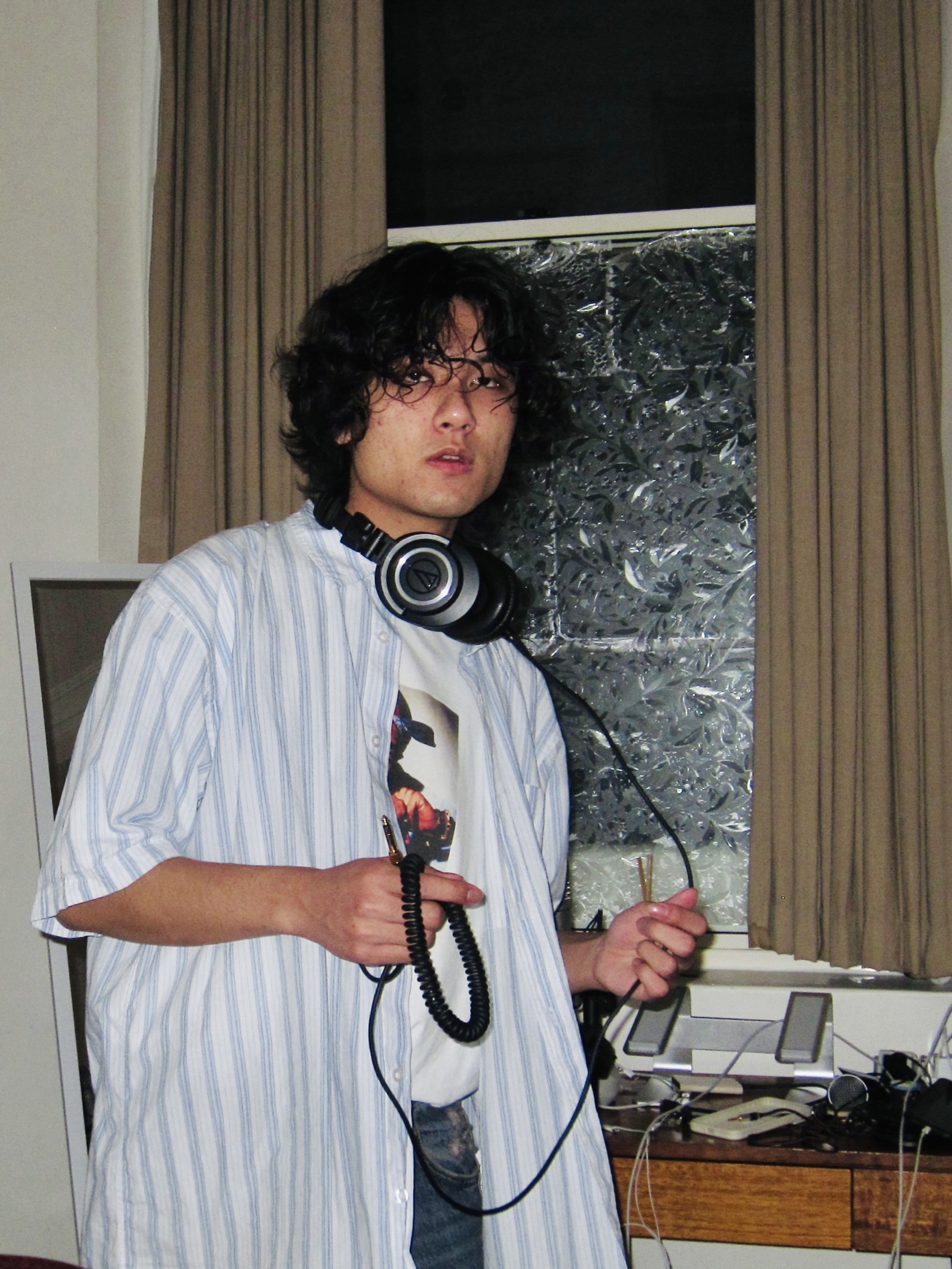 KUMA holding a headphone cable beside a window.